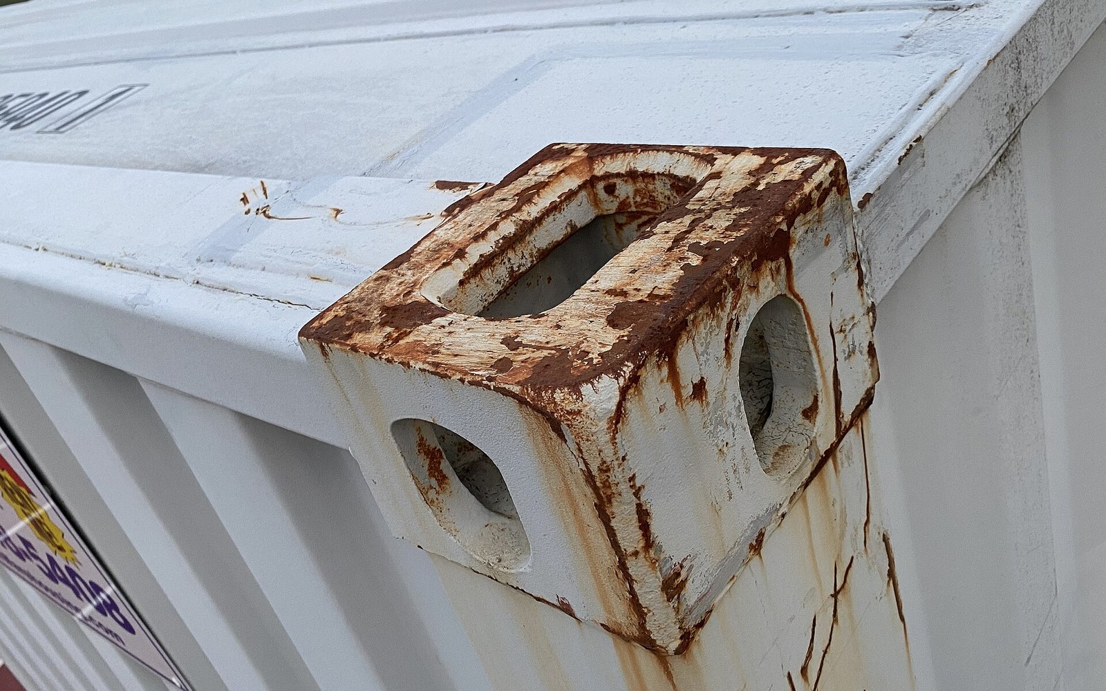 Rust streaks across a shipping container's corner casting with its twistlock aperture